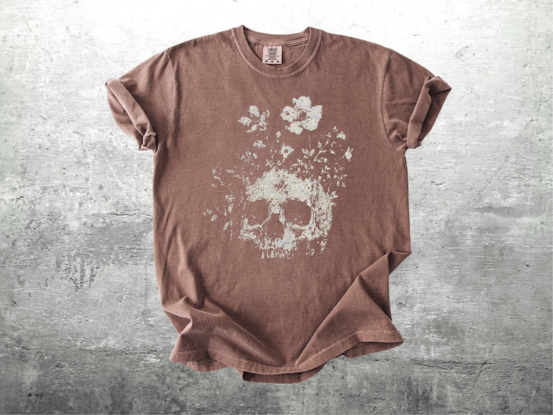Pu&ograve; includere: T-shirt marrone con un design a teschio invecchiato con dettagli floreali. La grafica &egrave; in bianco sbiadito, creando un'estetica vintage. La maglietta ha un girocollo e maniche corte.