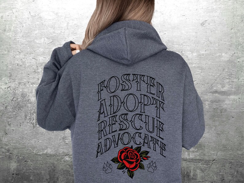 Pu&ograve; includere: Una felpa con cappuccio grigio scuro con il testo "FOSTER ADOPT RESCUE ADVOCATE" stampato in nero sul retro. Una rosa rossa con foglie verdi e due impronte di zampa si trovano sotto il testo.