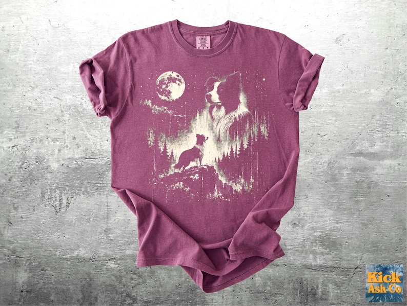 Pu&ograve; includere: T-shirt bordeaux con grafica di un cane sotto la luna piena e le stelle. Il design presenta una sagoma di cane, la testa di un cane pi&ugrave; grande e un cane pi&ugrave; piccolo su una collina, con alberi sullo sfondo.