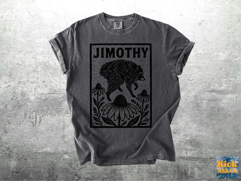 Peut inclure: Un t-shirt gris anthracite &agrave; manches courtes avec une impression graphique noire repr&eacute;sentant un raton laveur sautant au-dessus de grandes fleurs. Le texte JIMOTHY est imprim&eacute; en gras, en noir, au sommet du cadre rectangulaire central.