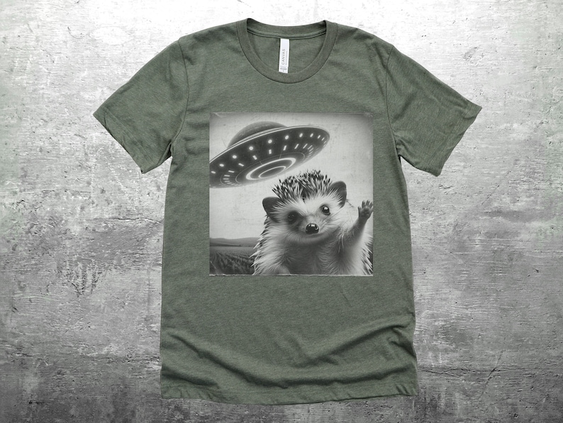 May include: A green t-shirt with a black and white image of a hedgehog waving at a flying saucer.
