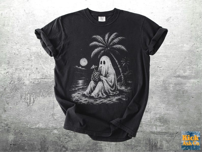 May include: A black short-sleeve t-shirt featuring a white graphic illustration of a ghost sitting on a beach under a palm tree at night. The ghost is holding a pineapple drink with a small umbrella. A full moon is visible in the sky above the water.