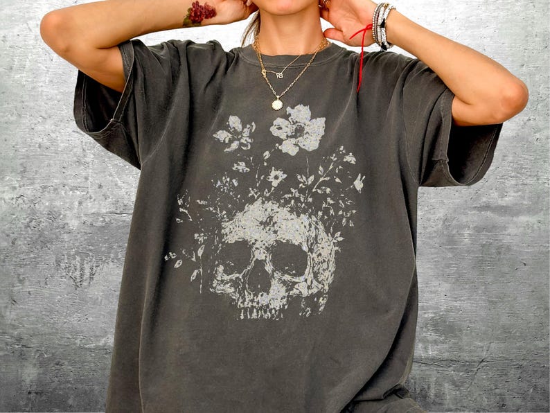 Pu&ograve; includere: T-shirt grigio scuro con un design a teschio e fiori bianchi. La stampa grafica bianca contrasta con il tessuto grigio. La maglietta ha maniche corte e una vestibilit&agrave; ampia, ideale per un abbigliamento casual.