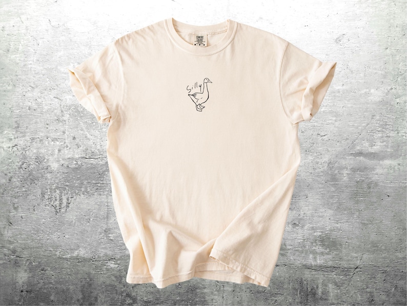 May include: A cream colored t-shirt with a black line drawing of a goose and the word "Silly" above it.