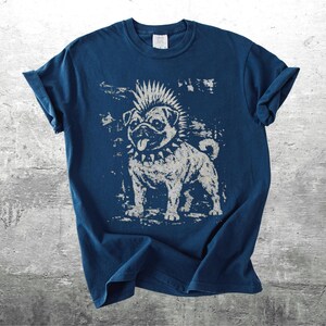 May include: A navy blue t-shirt featuring a distressed graphic of a punk rock pug dog with a mohawk and studded collar. The dog is in a standing pose, with its tongue sticking out. The shirt has rolled-up sleeves.