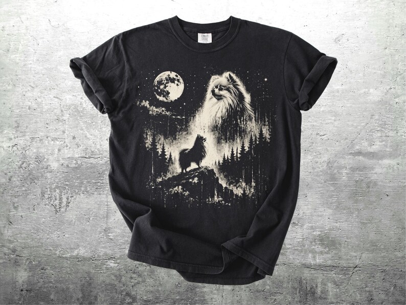 May include: Black t-shirt featuring a detailed graphic of a Pomeranian dog howling at the moon. The design includes a full moon, trees, and stars, creating a night scene. The shirt is made of a soft material.