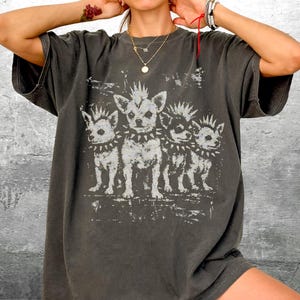 May include: Dark grey t-shirt featuring a distressed graphic of three chihuahua dogs with spiked collars. The dogs have mohawk-style haircuts. The shirt has short sleeves and a relaxed fit.