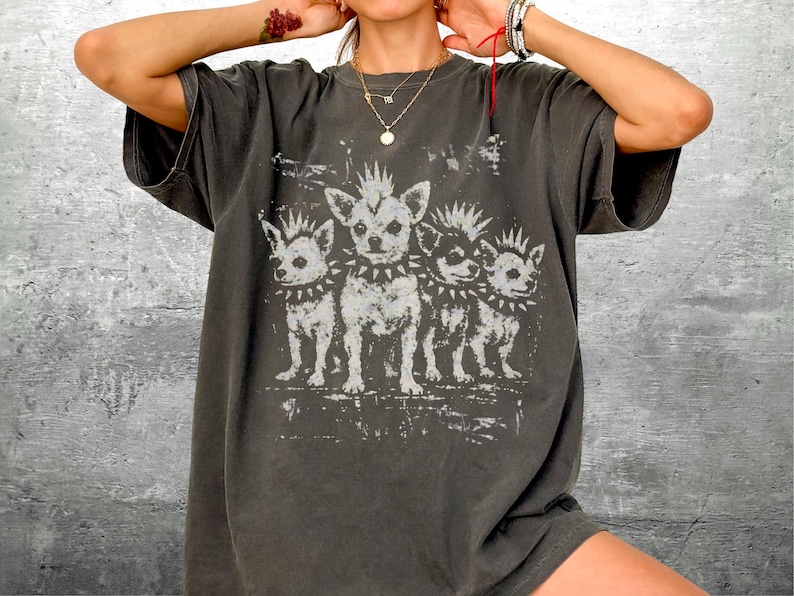 May include: Dark grey t-shirt featuring a distressed graphic of three chihuahua dogs with spiked collars. The dogs have mohawk-style haircuts. The shirt has short sleeves and a relaxed fit.