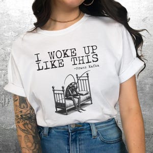 May include: White t-shirt with a black and white illustration of a cockroach in a bed. The text on the shirt reads "I woke up like this - Franz Kafka".