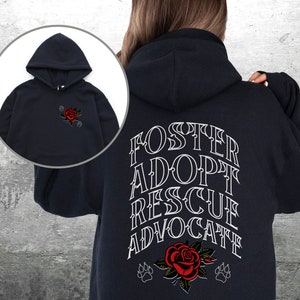 Pu&ograve; includere: Felpa con cappuccio nera con una grafica bianca sul retro che dice "Foster Adopt Rescue Advocate" con una rosa rossa e impronte di zampe. La parte anteriore della felpa ha una piccola grafica di rosa rossa.