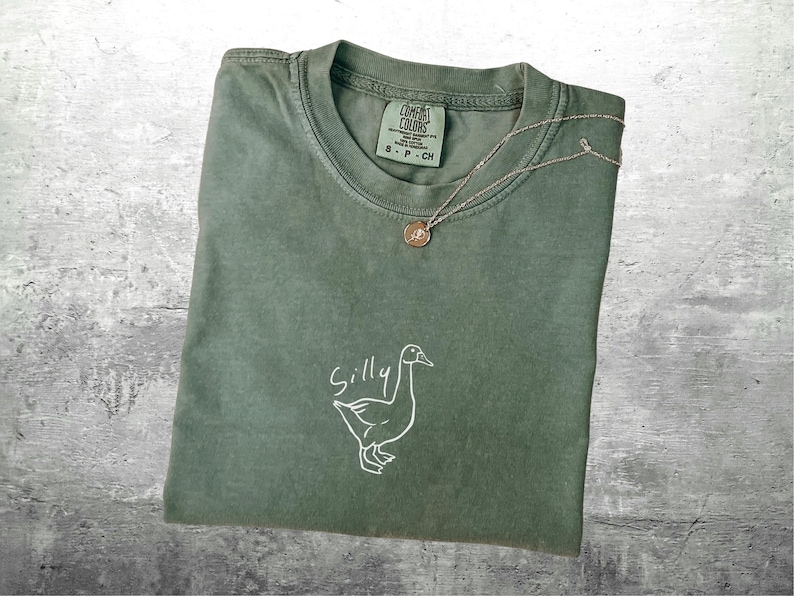 May include: A green t-shirt with a white outline of a goose and the word "Silly" written above it.