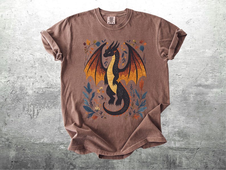 May include: A brown t-shirt with a black dragon with orange and yellow wings and floral details printed on the front.