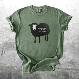 Puede incluir: Camiseta verde oliva con un dise&ntilde;o de oveja negra y el texto &laquo;EMBRACE WHAT MAKES YOU UNIQUE&raquo;. La camiseta tiene cuello redondo y mangas cortas, con pu&ntilde;os enrollados. La tela parece suave y c&oacute;moda, adecuada para el uso diario.