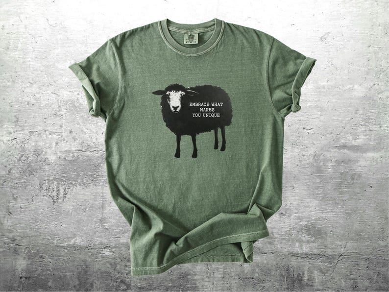 Puede incluir: Camiseta verde oliva con un dise&ntilde;o de oveja negra y el texto &laquo;EMBRACE WHAT MAKES YOU UNIQUE&raquo;. La camiseta tiene cuello redondo y mangas cortas, con pu&ntilde;os enrollados. La tela parece suave y c&oacute;moda, adecuada para el uso diario.