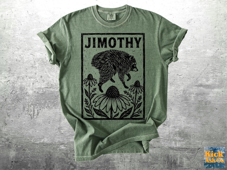Peut inclure: Un t-shirt &agrave; manches courtes vert sauge avec une impression graphique noire repr&eacute;sentant un raton laveur marchant au-dessus d'une grande fleur. Le texte JIMOTHY est imprim&eacute; en lettres capitales grasses en haut du cadre rectangulaire floral.