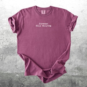 May include: A maroon t-shirt with the text "forever dilly dallying" printed in white on the front.
