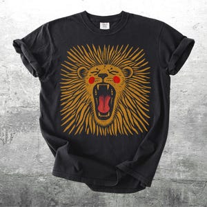 May include: Black t-shirt with a roaring lion design. The lion has a golden mane, red mouth, and pink cheeks. The design is centered on the shirt, with the sleeves rolled up. The shirt is made of a soft material.