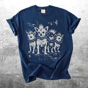 May include: Navy blue t-shirt featuring a distressed graphic of four chihuahua dogs with mohawks and studded collars. The dogs are in a row, with a vintage, punk rock aesthetic. The shirt has a classic crew neck and short sleeves.