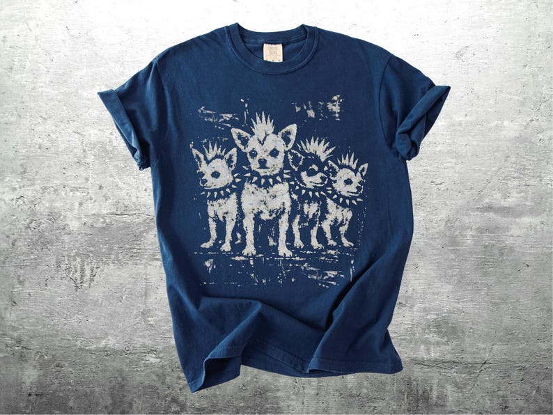 May include: Navy blue t-shirt featuring a distressed graphic of four chihuahua dogs with mohawks and studded collars. The dogs are in a row, with a vintage, punk rock aesthetic. The shirt has a classic crew neck and short sleeves.