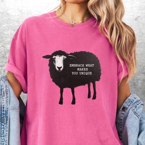 Puede incluir: Camiseta rosa brillante con un dise&ntilde;o de oveja negra y el texto "EMBRACE WHAT MAKES YOU UNIQUE". La camiseta tiene mangas cortas y un corte holgado, ideal para uso casual.