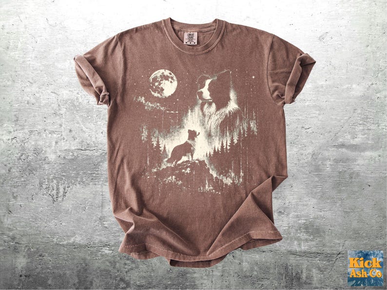 Pu&ograve; includere: T-shirt marrone con una grafica di un cane in una foresta sotto la luna piena. Il design include la silhouette di un cane su una collina, il volto di un cane pi&ugrave; grande e alberi. La maglietta ha un aspetto vintage.