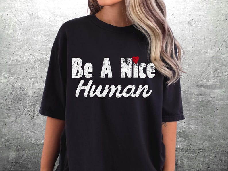 K&ouml;nnte beinhalten: Schwarzes T-Shirt mit dem wei&szlig;en, verwitterten Schriftzug "Be A Nice Human". Ein kleines rotes Herz befindet sich &uuml;ber dem Wort "Nice". Das Shirt hat einen l&auml;ssigen Stil.