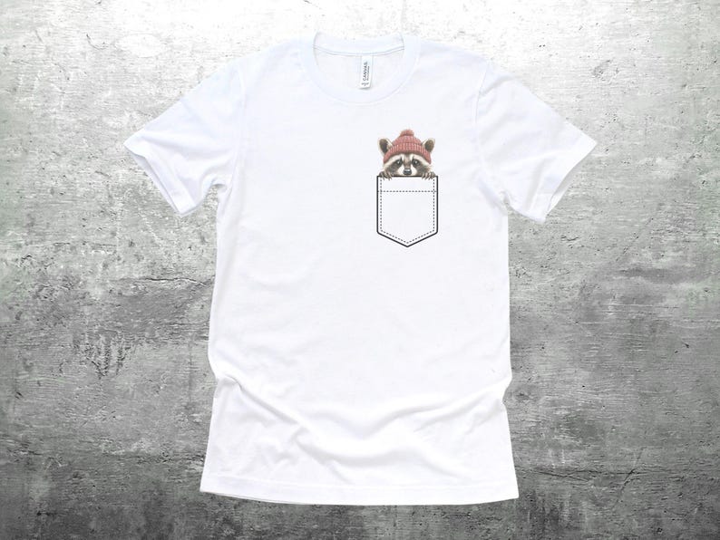 May include: White t-shirt with a pocket featuring a raccoon wearing a pink beanie hat.