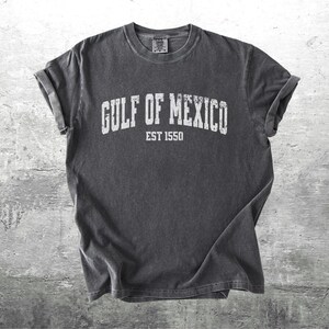 May include: A dark gray t-shirt with a white vintage-style graphic that reads "GULF OF MEXICO EST 1550".