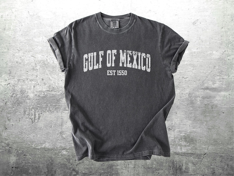 May include: A dark gray t-shirt with a white vintage-style graphic that reads "GULF OF MEXICO EST 1550".
