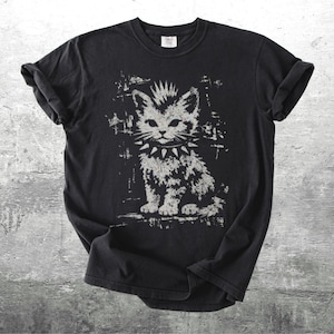 May include: Black t-shirt featuring a distressed graphic of a cat with a mohawk and spiked collar. The cat is depicted in shades of gray and white, with a punk rock aesthetic. The shirt has rolled-up sleeves and a classic crew neck.
