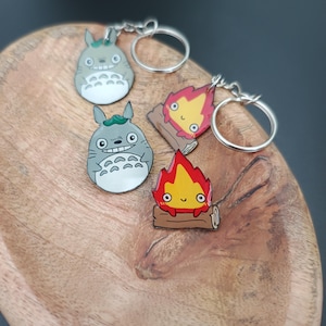 Può includere: Portachiavi con personaggi dei film d'animazione "Il mio vicino Totoro" e "Il castello errante". I portachiavi includono due figure di Totoro grigie e due demoni di fuoco Calcifer. Ogni portachiavi ha un anello color argento.