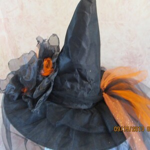 May include: Black witch hat with orange and black tulle accents. The hat has a tall pointed crown and a wide brim. The tulle is gathered into a large bow on the top of the hat.