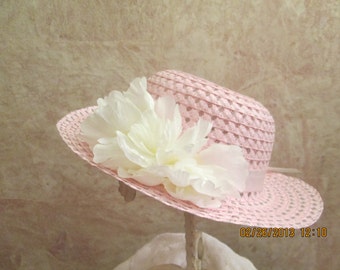 May include: A pink straw hat with a white flower accent. The hat has a woven design and a wide brim.