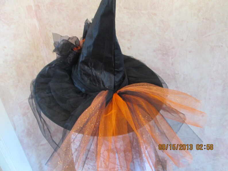 May include: Black witch hat with a black tulle veil and orange tulle trim. The hat has a pointed crown and a wide brim.