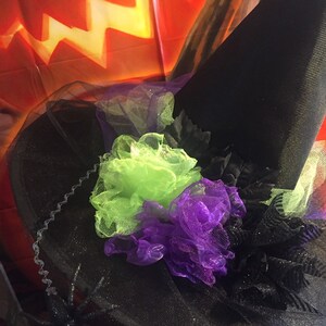 May include: Black witch hat with green and purple tulle flowers and a black spider on the brim.