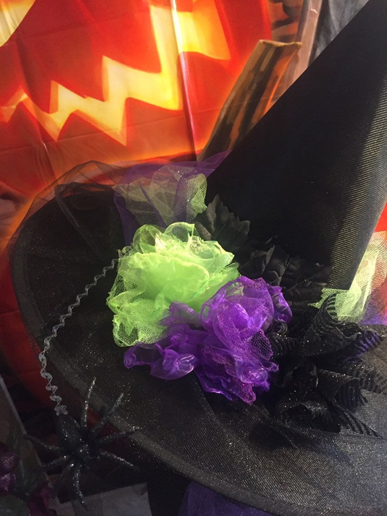 May include: Black witch hat with green and purple tulle flowers and a black spider on the brim.