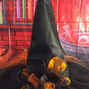 May include: A black witch's hat with a wide brim and a tall pointed crown. The hat is decorated with orange and brown tulle and a large orange bow.