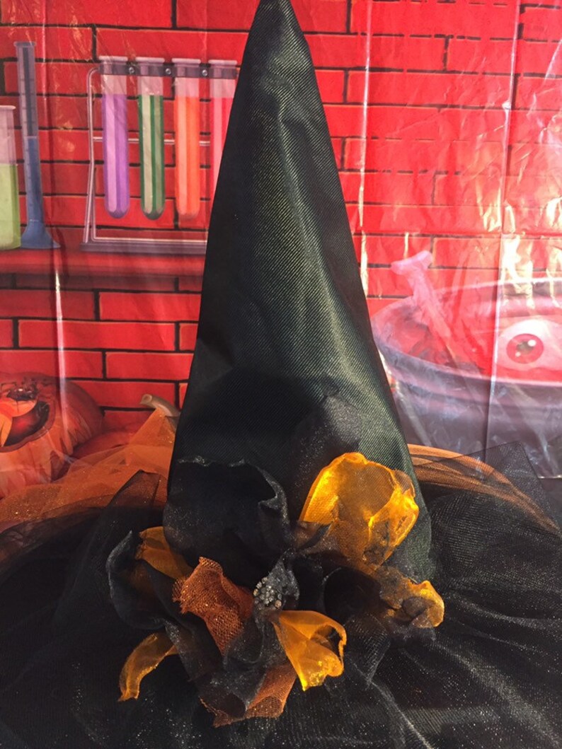 May include: A black witch's hat with a wide brim and a tall pointed crown. The hat is decorated with orange and brown tulle and a large orange bow.