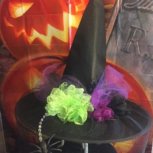 May include: Black witch hat with a wide brim, decorated with purple and green tulle, a green flower, and a black spider with silver beads.