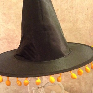 May include: A black witch hat with a wide brim and orange pom-poms around the edge.