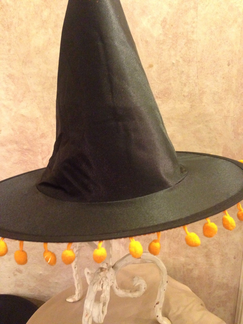 May include: A black witch hat with a wide brim and orange pom-poms around the edge.