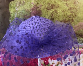 May include: A purple hat with a polka dot veil, sitting on a white stand in front of a field of pink and white tulips.