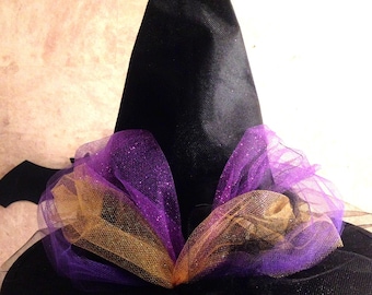 May include: A black witch's hat with a tall pointed crown and a wide brim. The hat is decorated with purple and gold tulle.