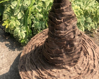May include: A brown fabric witch hat with a wide brim and a tall, pointed crown. The hat is made of many layers of fabric, giving it a textured look.
