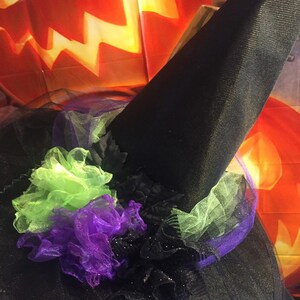 May include: A black witch's hat with a green and purple tulle bow. The hat is decorated with black glitter and is perfect for Halloween.