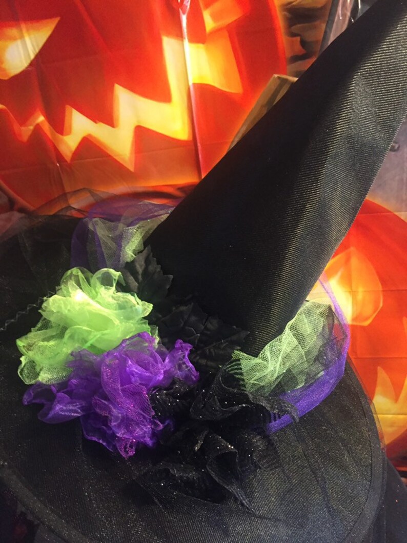 May include: A black witch's hat with a green and purple tulle bow. The hat is decorated with black glitter and is perfect for Halloween.