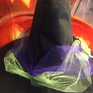 May include: A black witch hat with a purple and green tulle bow. The hat is decorated with a green and yellow flower.