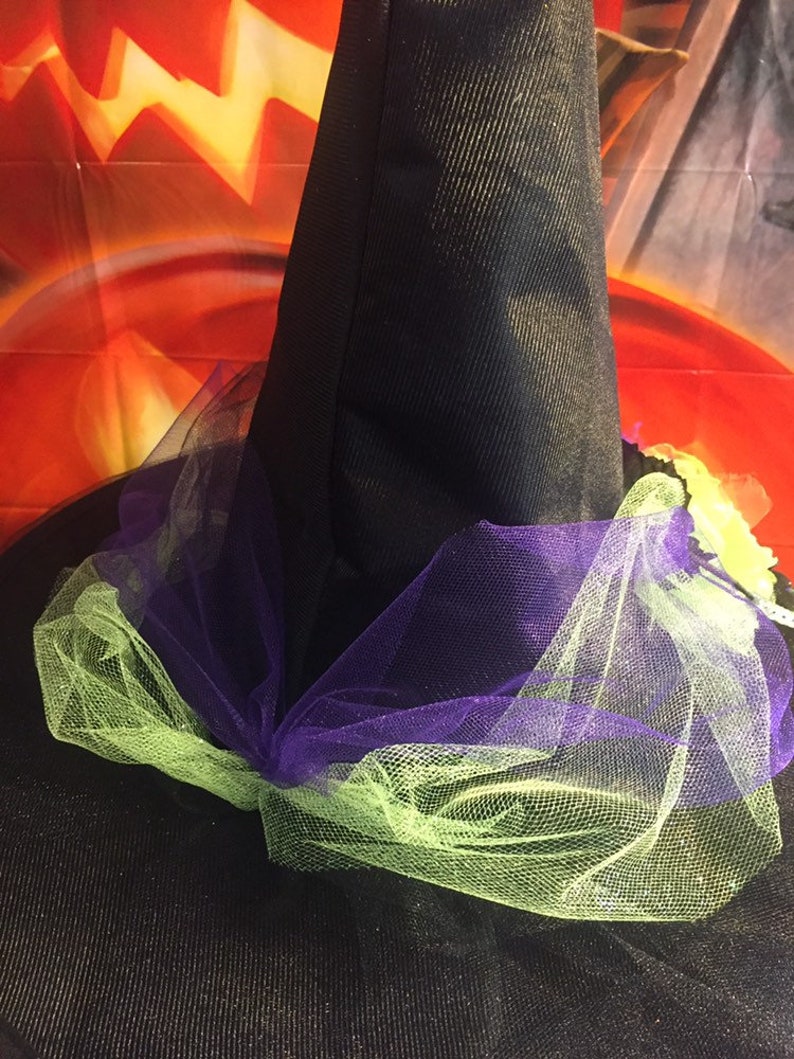 May include: A black witch hat with a purple and green tulle bow. The hat is decorated with a green and yellow flower.