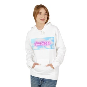 May include: White hooded sweatshirt with a front pocket and the word "Goddess" in pink neon lettering over a sky and cloud design. The model is wearing blue jeans.