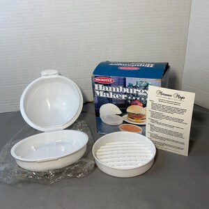 Puede incluir: Un juego blanco de Microtex Hamburger Maker, que incluye un recipiente para cocinar, una tapa y una bandeja ranurada. La caja presenta una imagen de una hamburguesa cocinada. También se incluye una tarjeta separada titulada "Microwave Magic".